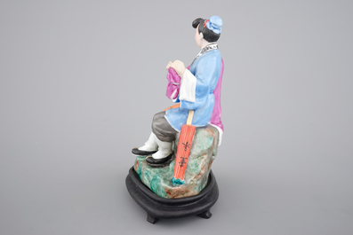 A Chinese porcelain model of an amorous couple, on wooden stand, 20th C.