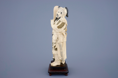 Een Chinese ivoren figuur van een strijder op houten sokkel, eind 19e eeuw