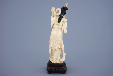 A Chinese carved ivory figure of Guanyin with a bird on wooden base, 19th C.