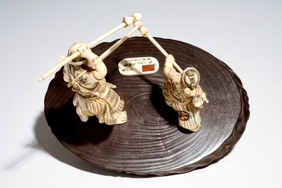 A Japanese ivory group of a warrior and his pupil, on a wooden base, Meiji, signed