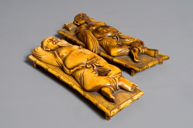 A pair of Chinese carved ivory figures of resting men on a bed, 19th C.