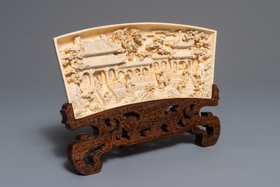 A Chinese carved ivory panel with figures in a landscape on inlaid wooden stand, first half 20th C.