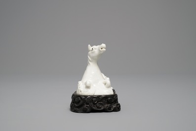 Een Chinees Dehua blanc de Chine model van een liggend paard op houten basis, Kangxi