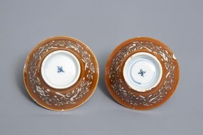 Une paire de tasses et soucoupes en porcelaine de Chine bleu et blanc &agrave; d&eacute;cor grav&eacute; sur fond brun capucin, Kangxi