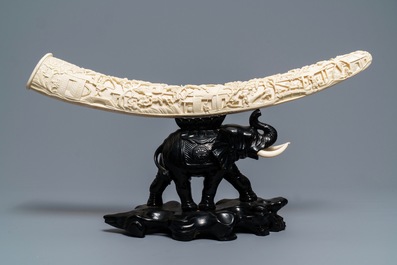 A Chinese carved ivory tusk on wooden elephant stand, ca. 1900