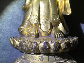 Een Chinese verguld bronzen figuur van een staande Boeddha met inscriptie, Qianlong