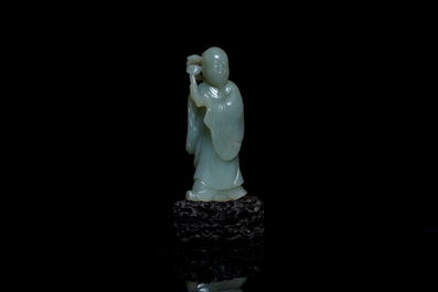 Een Chinese figuur van een onsterfelijke in celadon jade op houten sokkel, Qing