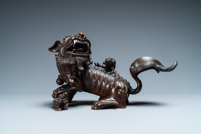 A Chinese bronze model of a Buddhist lion on a finely carved wooden stand, 18th C.