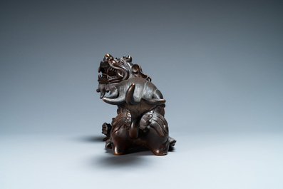 A Chinese bronze model of a Buddhist lion on a finely carved wooden stand, 18th C.