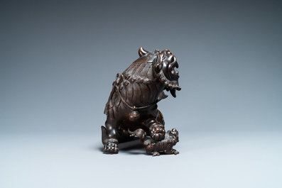 A Chinese bronze model of a Buddhist lion on a finely carved wooden stand, 18th C.