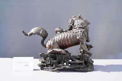 A Chinese bronze model of a Buddhist lion on a finely carved wooden stand, 18th C.