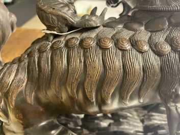 A Chinese bronze model of a Buddhist lion on a finely carved wooden stand, 18th C.