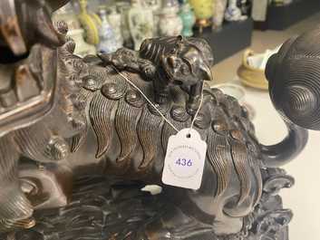 A Chinese bronze model of a Buddhist lion on a finely carved wooden stand, 18th C.