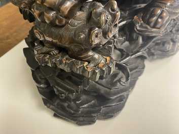 A Chinese bronze model of a Buddhist lion on a finely carved wooden stand, 18th C.