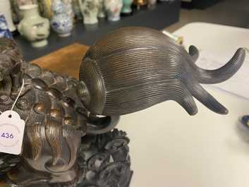 A Chinese bronze model of a Buddhist lion on a finely carved wooden stand, 18th C.