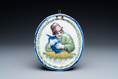 A polychrome Brussels faience oval molded plaque and a matching grisaille painting on copper of a man with a jug, early 19th C.