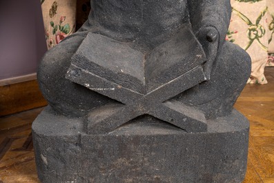 A basalt sculpture of a reading student, Indonesia, 20th C.