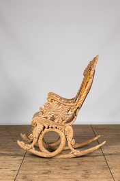 A richly carved wooden rocking chair with snake-shaped legs, 20th C.
