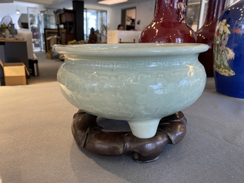 A Chinese celadon-glazed tripod censer with floral scrolls on wooden stand, Qing