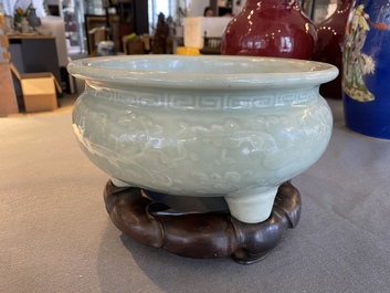 A Chinese celadon-glazed tripod censer with floral scrolls on wooden stand, Qing