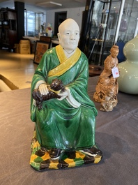 A Chinese verte biscuit figure of a Luohan holding a dog, probably Qing