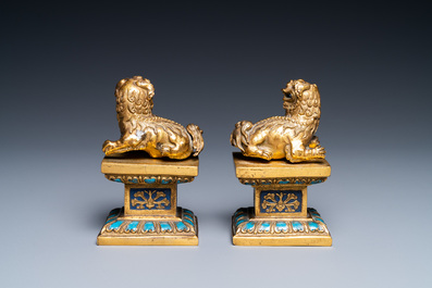A pair of Chinese gilt copper alloy Buddhist lions on champlev&eacute; enamel bases, 19th C.