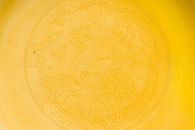 A pair of Chinese monochrome yellow-glazed saucers with incised designs of pine and cranes, Yongzheng mark and of the period