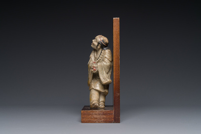 A Chinese partly polychromed soapstone figure on a wooden stand, 18th C.