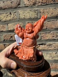 A Chinese red coral figure of a laughing Buddha on wooden stand, 19/20th C.