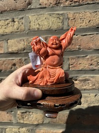 A Chinese red coral figure of a laughing Buddha on wooden stand, 19/20th C.