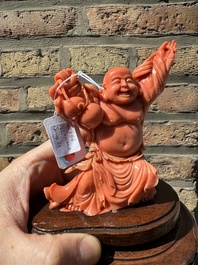 A Chinese red coral figure of a laughing Buddha on wooden stand, 19/20th C.