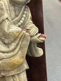 A Chinese partly polychromed soapstone figure on a wooden stand, 18th C.