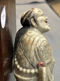 A Chinese partly polychromed soapstone figure on a wooden stand, 18th C.