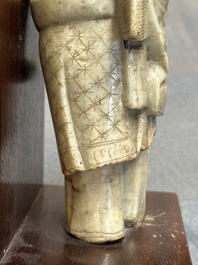 A Chinese partly polychromed soapstone figure on a wooden stand, 18th C.