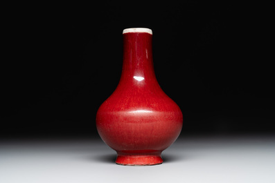 Two Chinese monochrome copper-red-glazed bottle vases on wooden stands, 19th C.