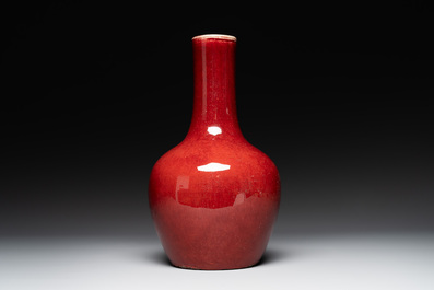 Two Chinese monochrome copper-red-glazed bottle vases on wooden stands, 19th C.