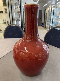 Two Chinese monochrome copper-red-glazed bottle vases on wooden stands, 19th C.