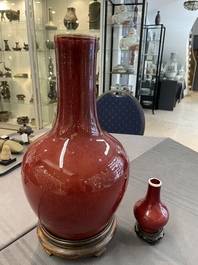 Two Chinese monochrome copper-red-glazed bottle vases on wooden stands, 19th C.