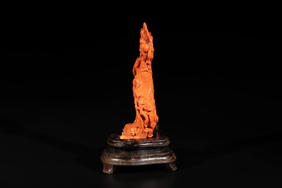 A Chinese red coral Guanyin holding a lotus on wooden stand, 19/20th C.
