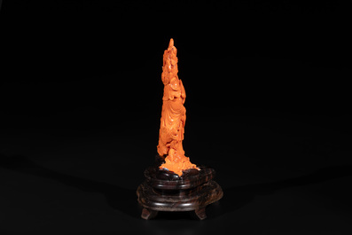 A Chinese red coral Guanyin holding a lotus on wooden stand, 19/20th C.