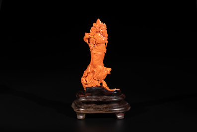 A Chinese red coral Guanyin holding a lotus on wooden stand, 19/20th C.