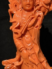 A Chinese red coral Guanyin holding a lotus on wooden stand, 19/20th C.