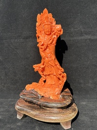 A Chinese red coral Guanyin holding a lotus on wooden stand, 19/20th C.