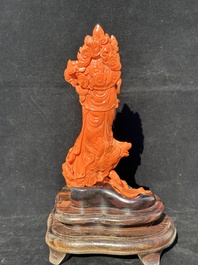 A Chinese red coral Guanyin holding a lotus on wooden stand, 19/20th C.