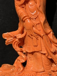 A Chinese red coral Guanyin holding a lotus on wooden stand, 19/20th C.