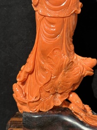 A Chinese red coral Guanyin holding a lotus on wooden stand, 19/20th C.