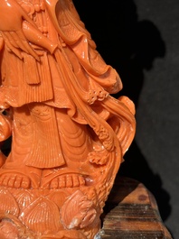 A Chinese red coral Guanyin holding a lotus on wooden stand, 19/20th C.