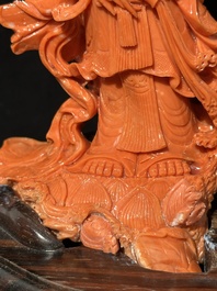 A Chinese red coral Guanyin holding a lotus on wooden stand, 19/20th C.