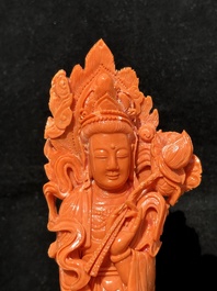 A Chinese red coral Guanyin holding a lotus on wooden stand, 19/20th C.