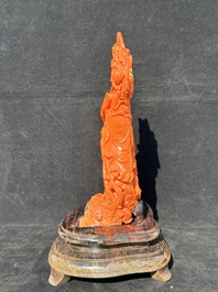 A Chinese red coral Guanyin holding a lotus on wooden stand, 19/20th C.